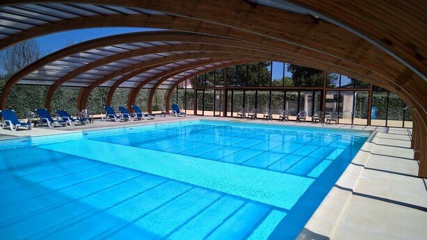 Una amplia piscina cubierta con agua cristalina, rodeada de vigas de madera y cubierta por un techo transparente.