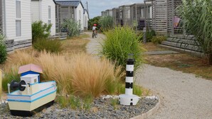Un camino que lleva a una hilera de casas móviles, con un pequeño bote y una estructura similar a un faro al frente.