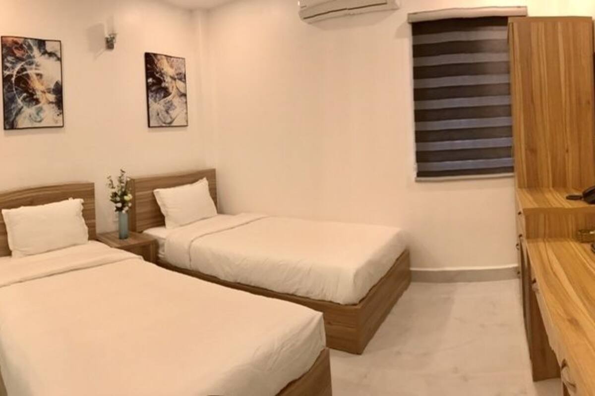 A hotel room with two beds, a wooden desk, a television, and artwork on the walls.