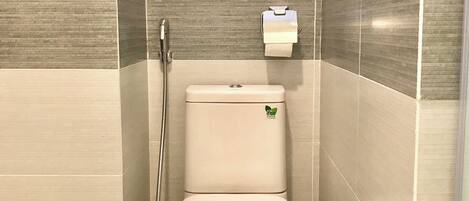 Une petite salle de bain fermée, équipée de toilettes, d’une douchette et d’un distributeur d’essuie-tout en papier.