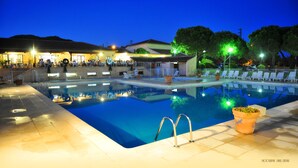 A swimming pool with a tiled deck, lounge chairs, and a building in the background. - Les Residences du Colombier - ULVF (Fréjus)