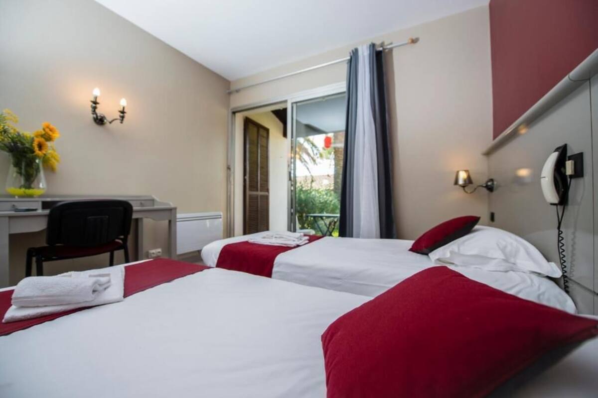 A hotel room with two beds, a desk, a chair, a phone, and a window with curtains.