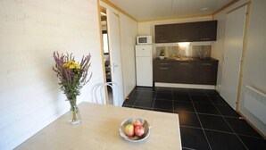 Una cocina compacta con armarios oscuros, un refrigerador blanco y un microondas. Un jarrón con flores y un cuenco de fruta están sobre la mesa.