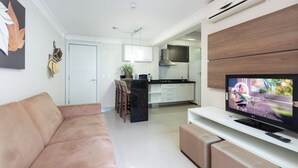 Een moderne woonkamer met een bank, een televisie en een keuken op de achtergrond.