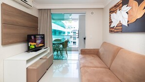 Een moderne woonkamer met een flatscreen televisie, een beige bank en een glazen schuindeur naar een buitenbalkon.