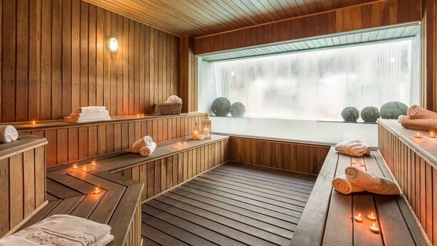 Een houten sauna met banken, kaarsen en uitzicht op bomen door een groot raam.
