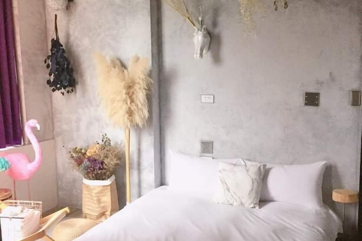 Quarto moderno com uma cama grande, uma mesa de cabeceira pequena, uma cadeira e um flamingo decorativo.