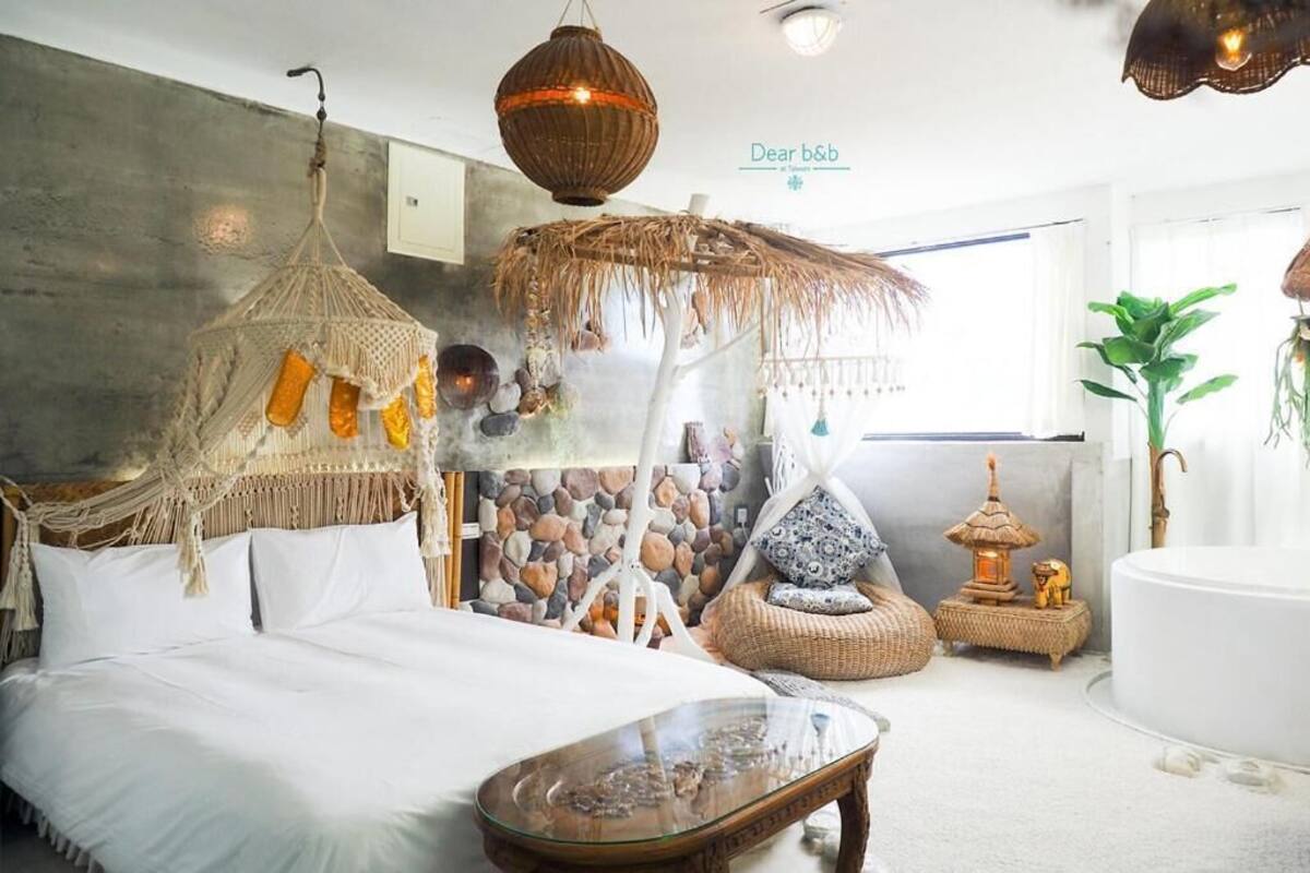 Quarto com cama, uma cadeira suspensa, mesa de centro de vidro, parede de pedra e um pequeno santuário.