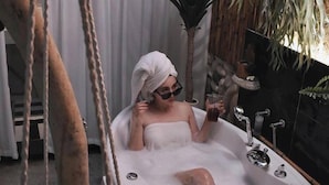 A person relaxing in a bathtub with a towel wrapped around their head, surrounded by plants and a hanging chair. - Fas Glass House B&B (Xincheng)