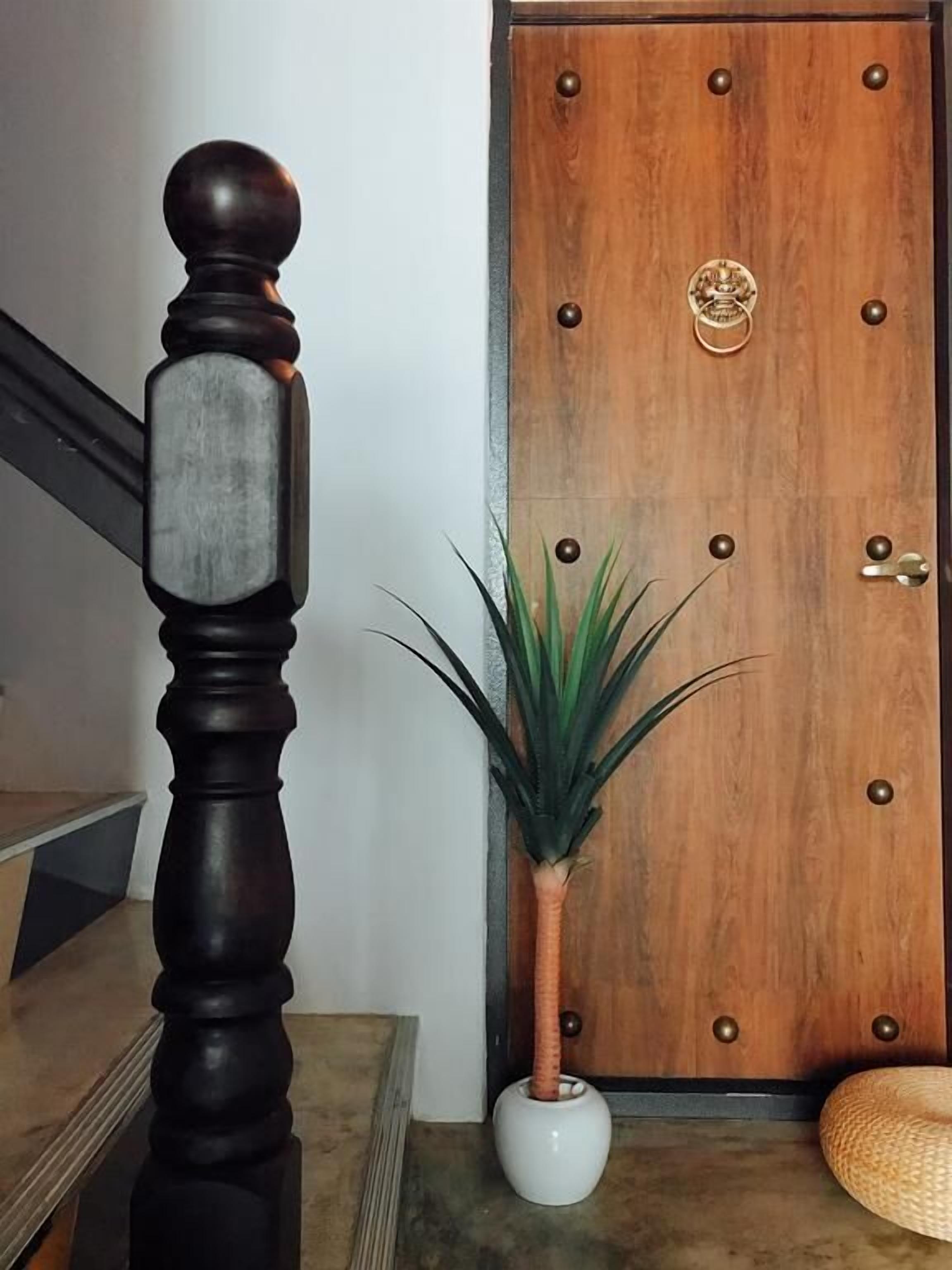 A wooden door with a brass knocker and a potted plant beside a staircase with a dark baluster.