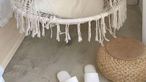 A macrame hanging chair with a cushion, a woven stool, and a pair of slippers on the floor. - Fas Glass House B&B (Xincheng)