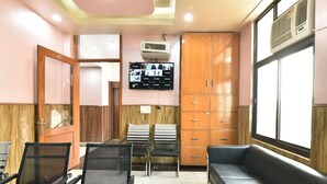 A waiting area with a reception desk, a sofa, and a television mounted on the wall. - Greno House (Greater Noida)