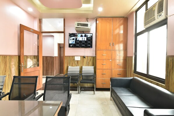 A waiting area with a reception desk, a sofa, and a television mounted on the wall. - Greno House (Greater Noida)