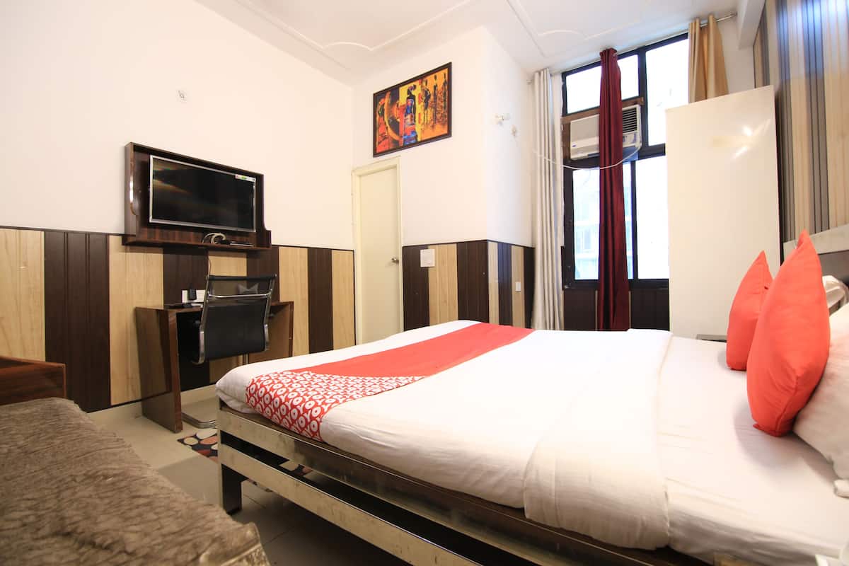 A hotel room with a bed, a TV, a desk, and a window with curtains.
