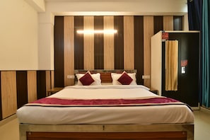 A hotel room with a wooden bed frame, a large window, and a wardrobe with a mirror. - Greno House (Greater Noida)