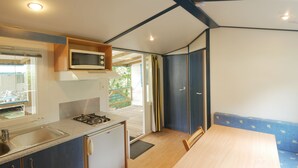 A compact kitchen with a microwave, sink, and small refrigerator. There is a wooden dining table with chairs and a view of a balcony through a door. - Ty an Diaoul - Vacances ULVF (Sarzeau)