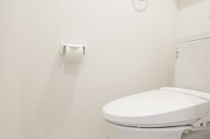 A white toilet with a flush handle and a paper towel holder on the wall. - Cozy Vibes Apartment Hotel (Tokyo)