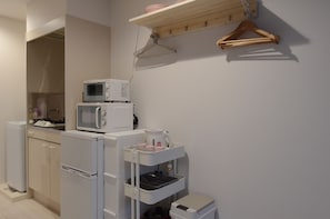 A compact kitchen with a microwave, a small refrigerator, and a white countertop with a tray holding kitchen items. - Cozy Vibes Apartment Hotel (Tokyo)