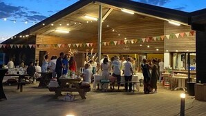 An outdoor dining area with a covered roof, wooden tables, and string lights. - La Grande Dune - Vacances ULVF (Saint-Hilaire-de-Riez)