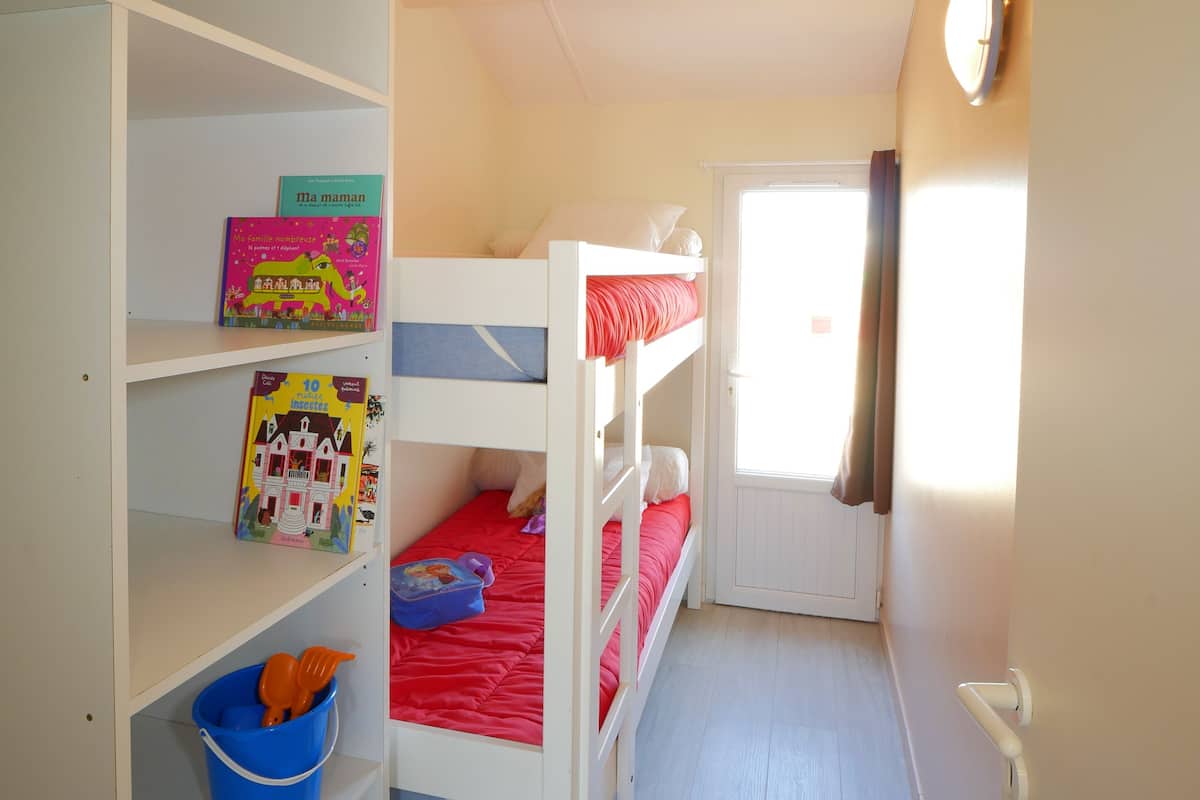 A bunk bed room with a window, a bookshelf, and a door.