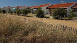 A row of single-story houses with red-tiled roofs, surrounded by dry grass and a wooden fence. - La Grande Dune - Vacances ULVF (Saint-Hilaire-de-Riez)