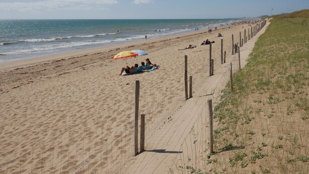 A sandy beach with a fence, umbrellas, and people relaxing. - La Grande Dune - Vacances ULVF (Saint-Hilaire-de-Riez)