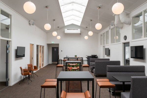 A conference room with a high ceiling, round pendant lights, a central table with chairs, and a large window on one side.