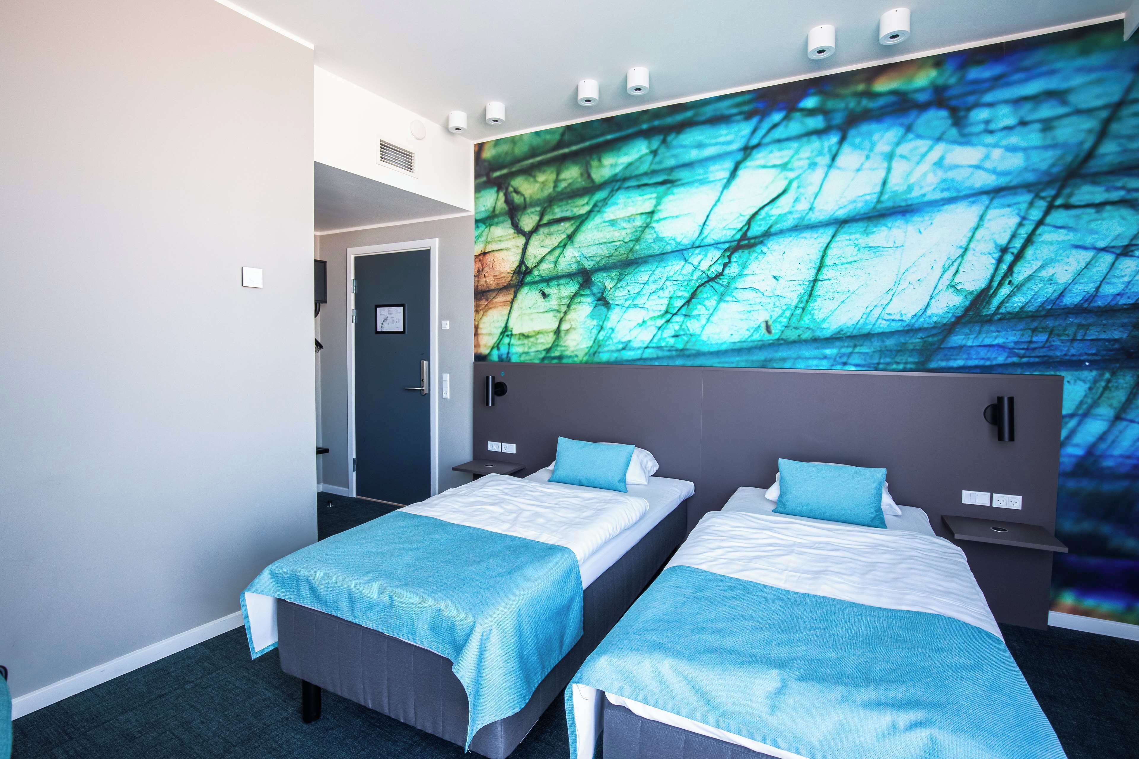A hotel room with two beds, a large abstract mural on the wall, and a door leading to another room.