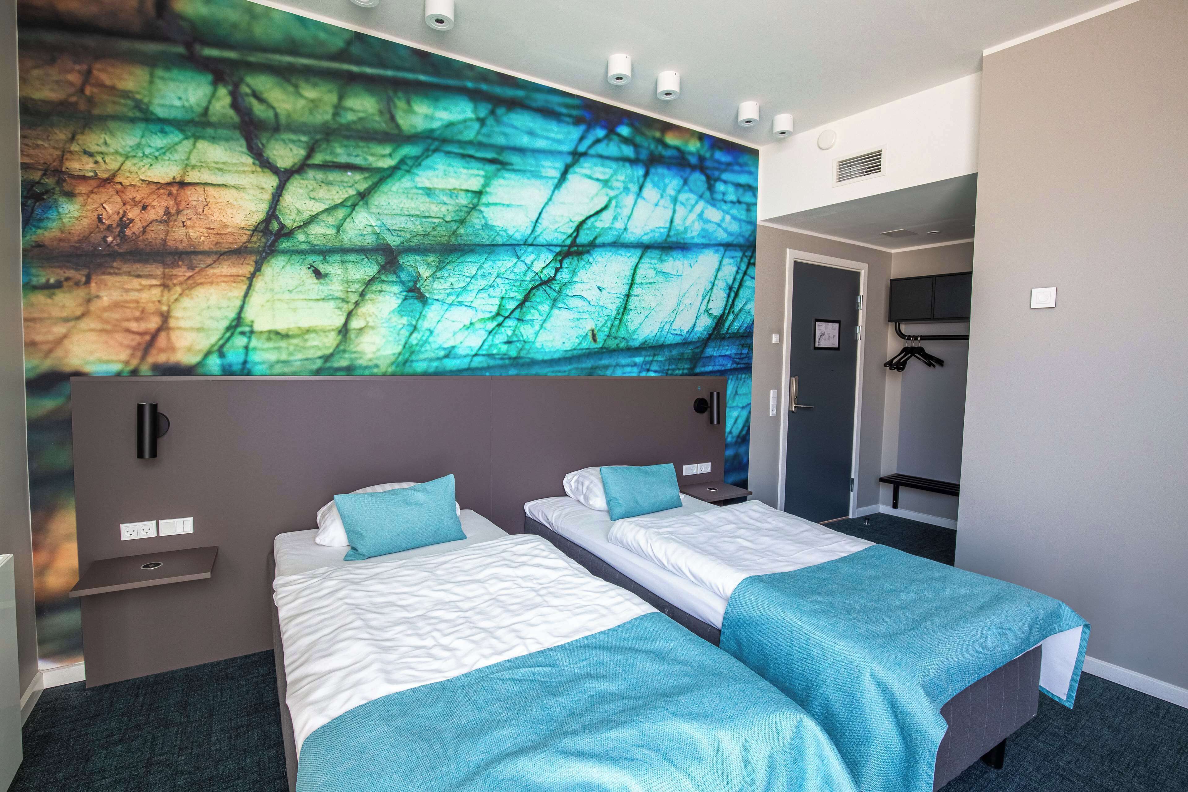A hotel room with two beds, a large abstract wall art, a wardrobe, and a coat rack.