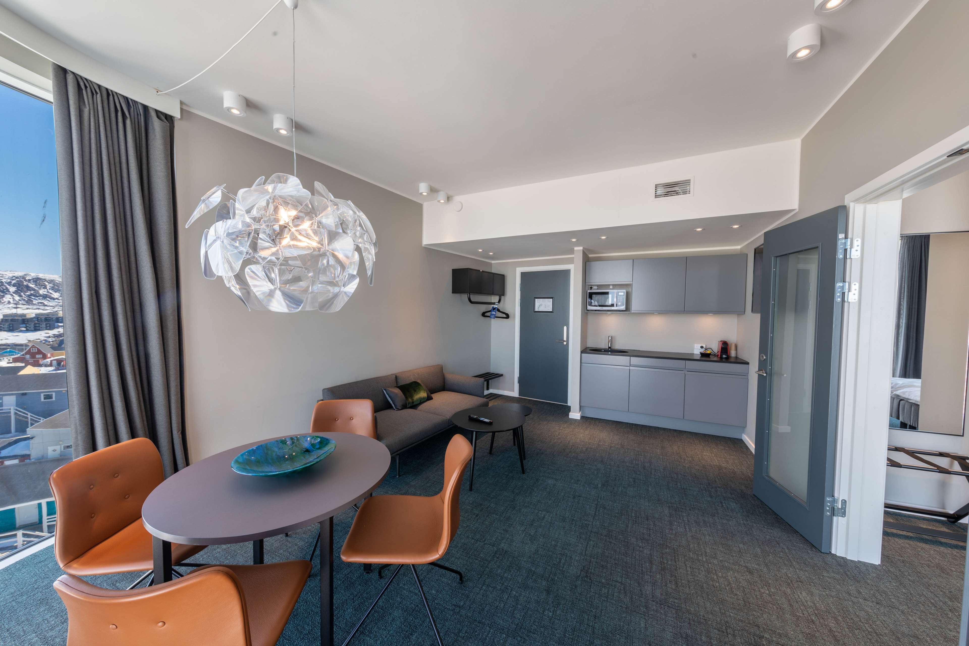 A modern hotel room with a dining area, a sofa, and a kitchen.