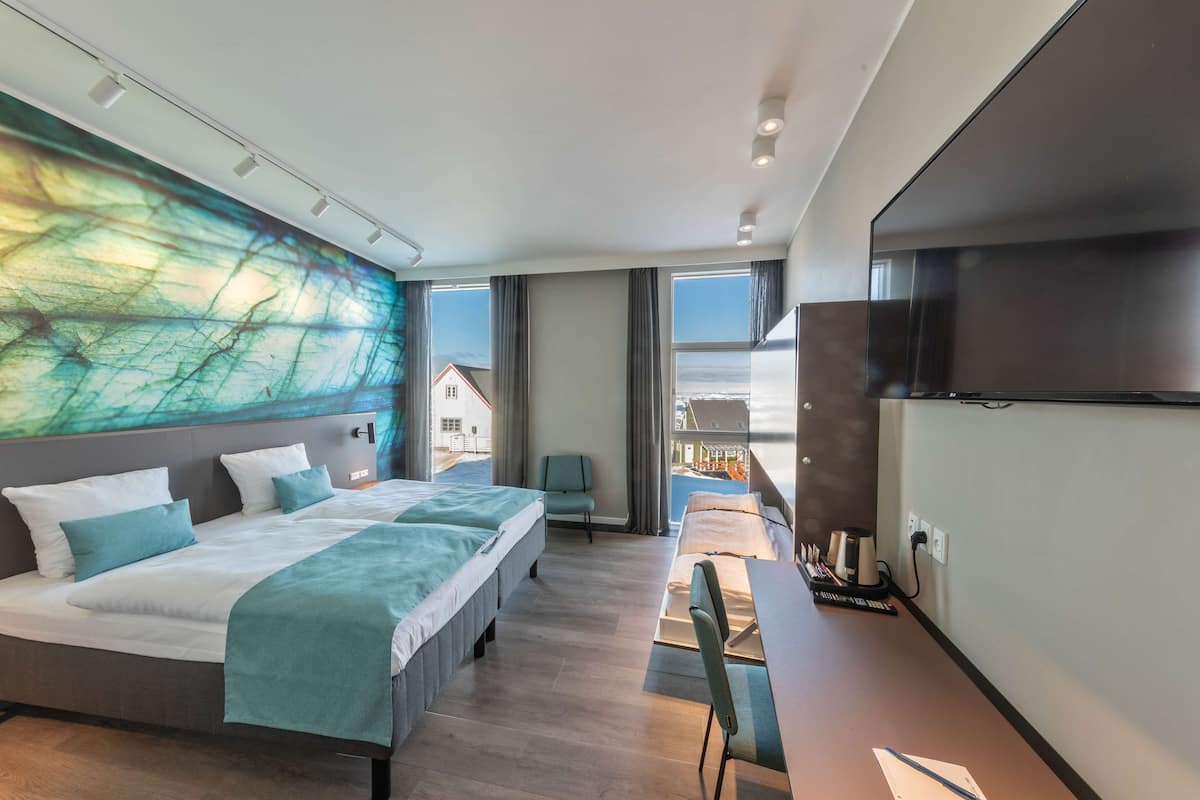 Ein modernes Hotelzimmer mit einem großen Bett, einem Schreibtisch und einem Fernseher. Es bietet einen Blick auf ein Gebäude.