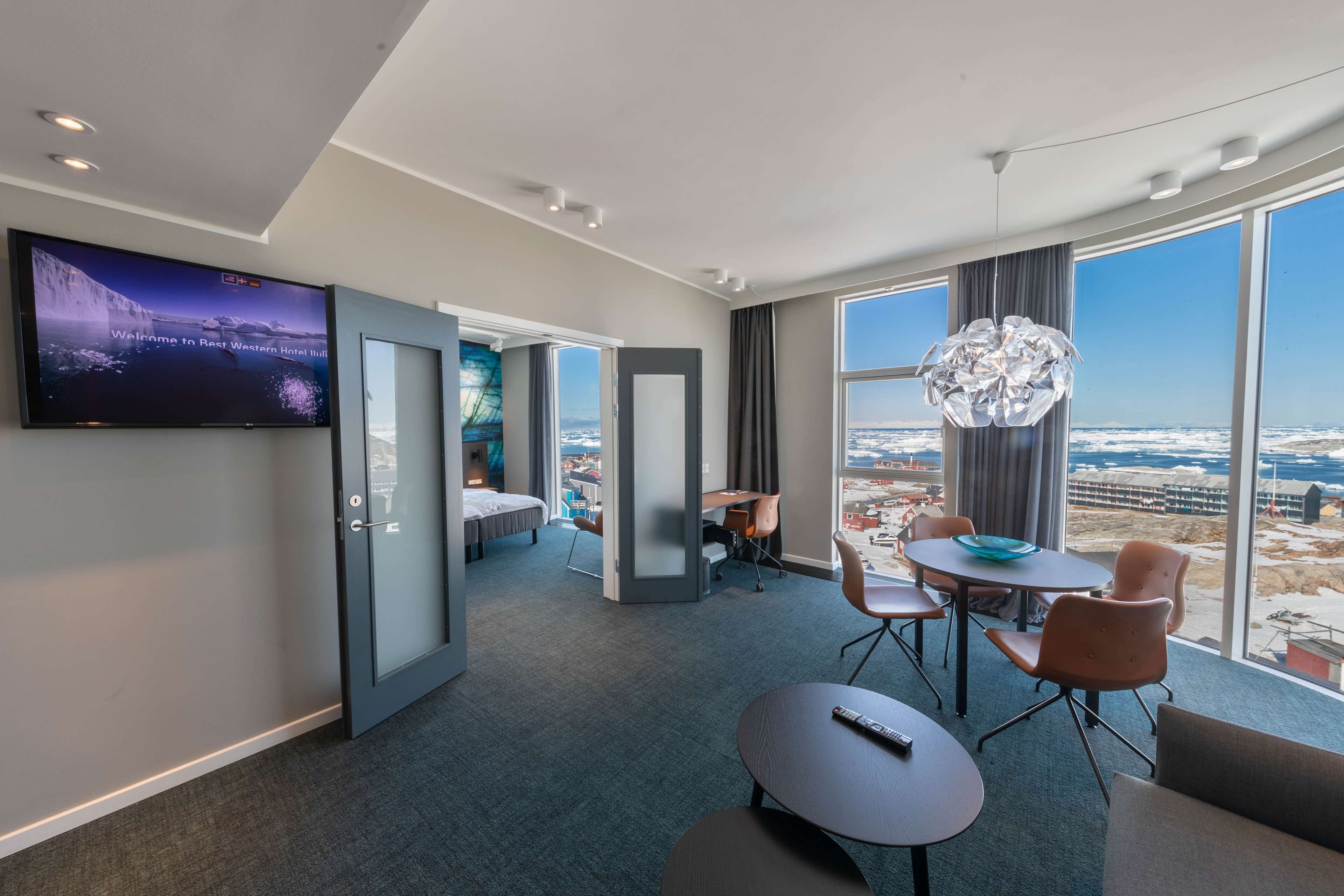 Ein modernes Hotelzimmer mit großem Fernseher, einer Essecke mit Blick und einer gemütlichen Sitzecke.