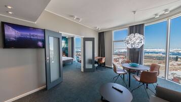 Ein modernes Hotelzimmer mit großem Fernseher, einer Essecke mit Blick und einer gemütlichen Sitzecke.