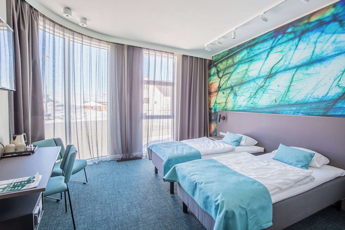 Ein Hotelzimmer mit zwei Betten, einem Schreibtisch und einem großen Fenster mit Vorhängen.
