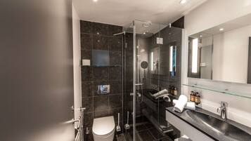 A modern bathroom with a glass-enclosed shower, a white toilet, a black sink with a glass countertop, and a large mirror above the sink.