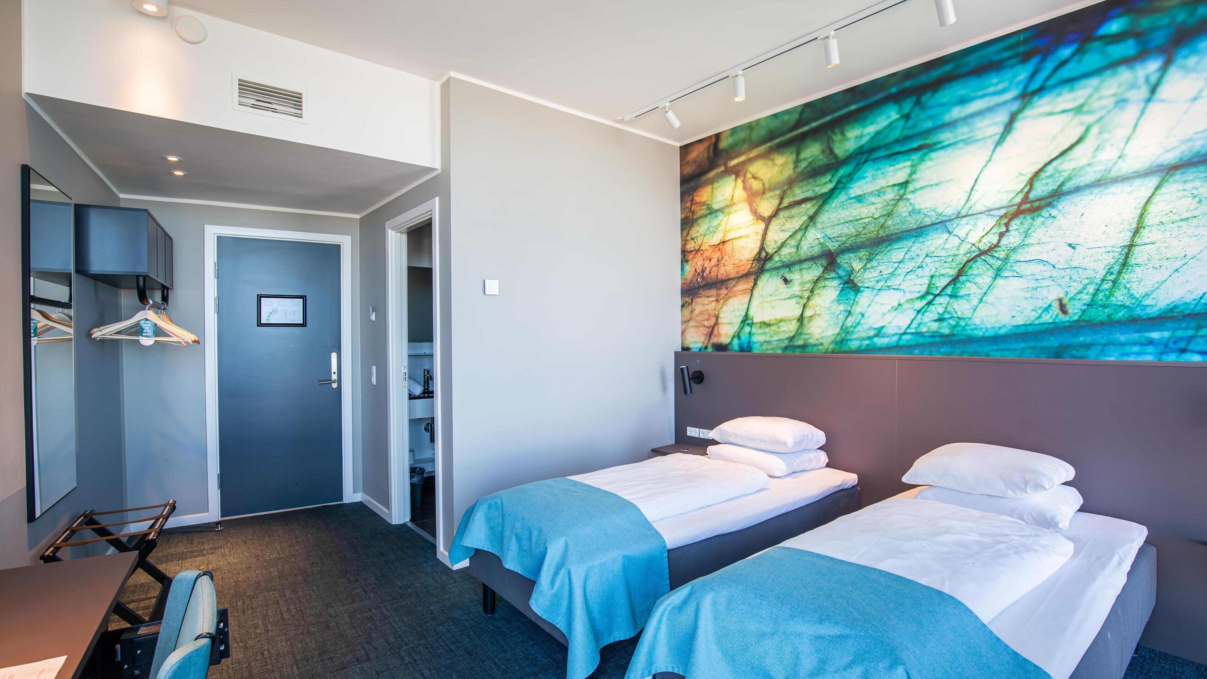 A hotel room with two beds, a large abstract painting on the wall, and a desk with a chair.