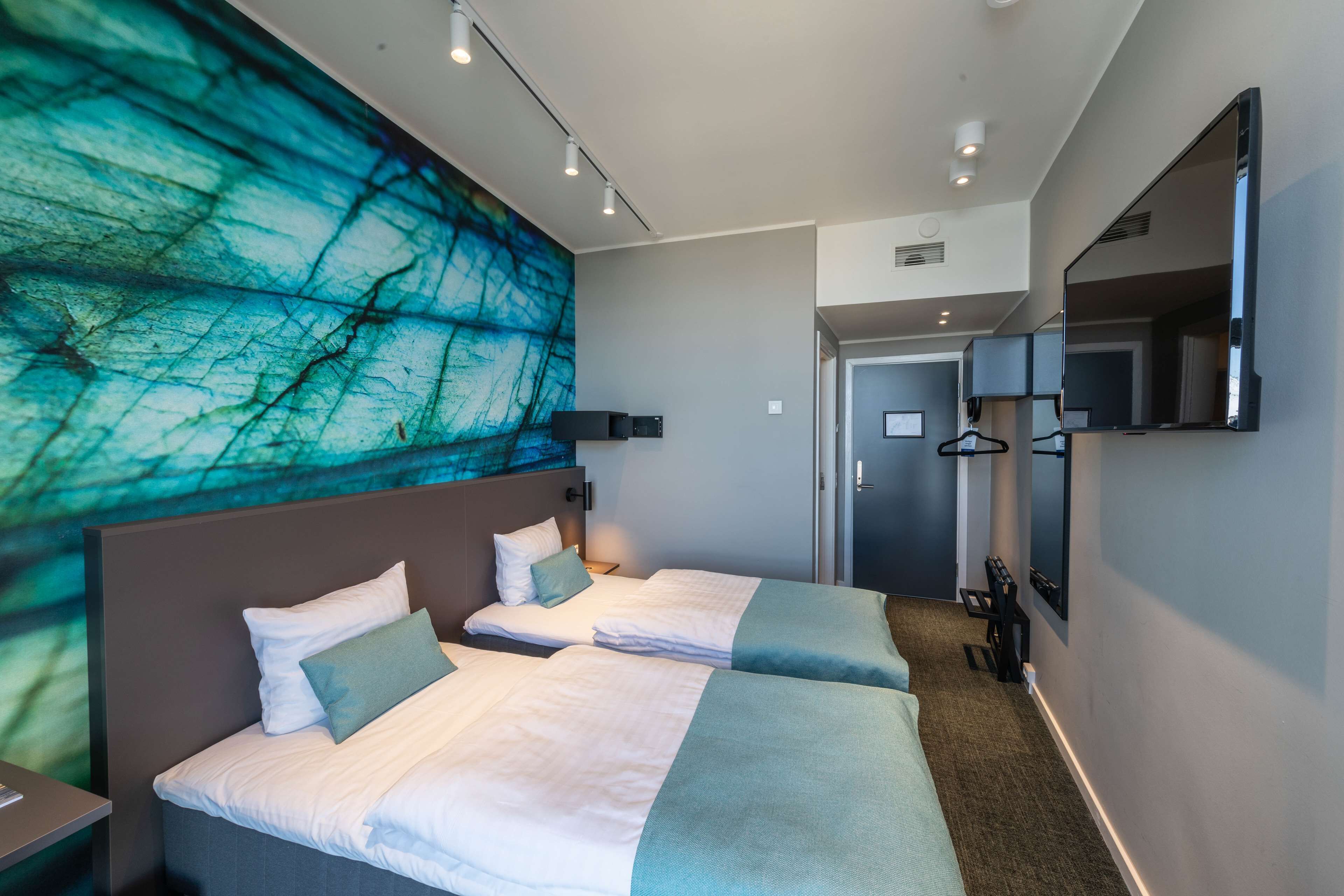 A hotel room with two beds, a large abstract mural, a wardrobe, and a mirror.