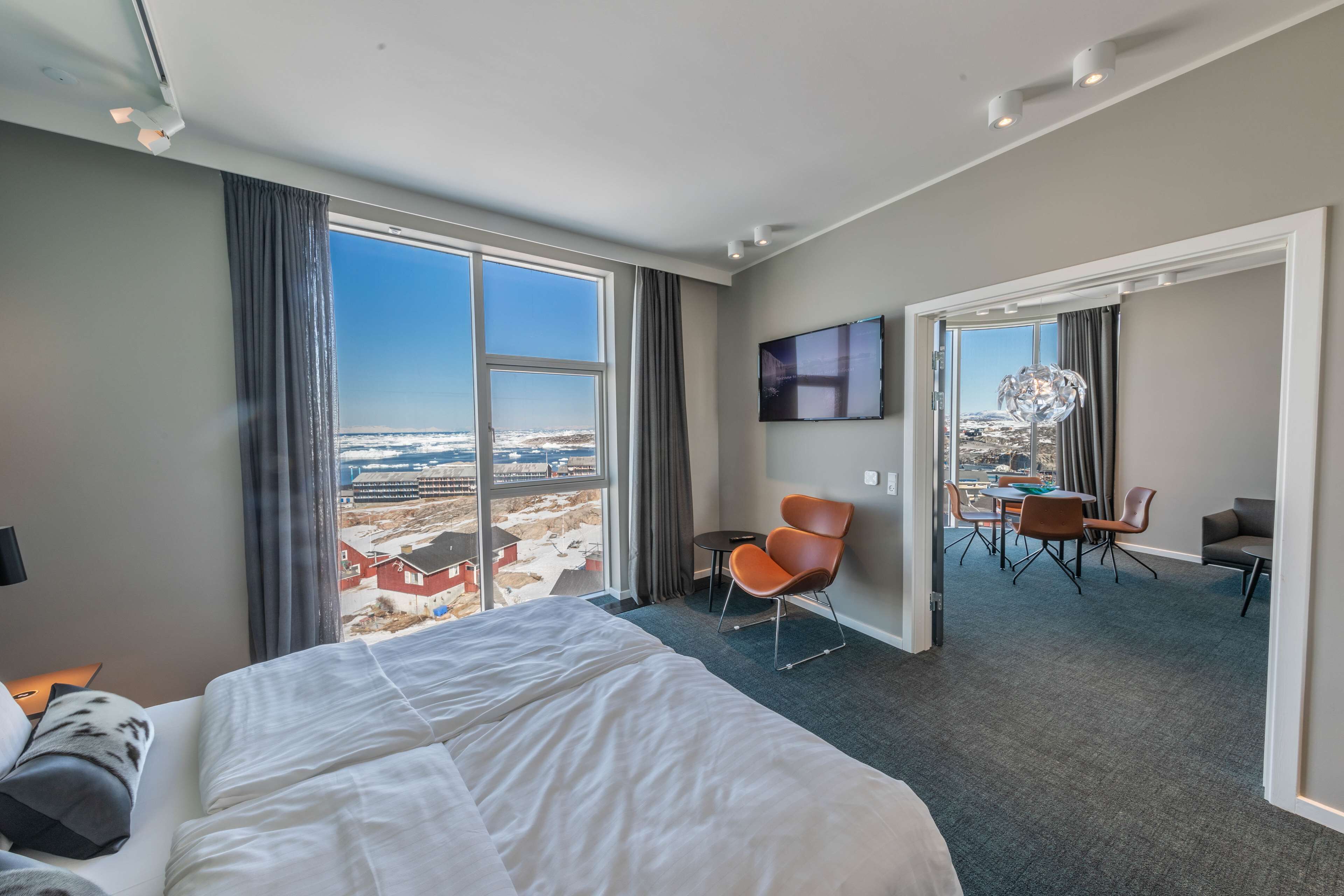 Habitación de hotel con una cama grande, un escritorio y una silla. Se ve la ciudad a través de la ventana.