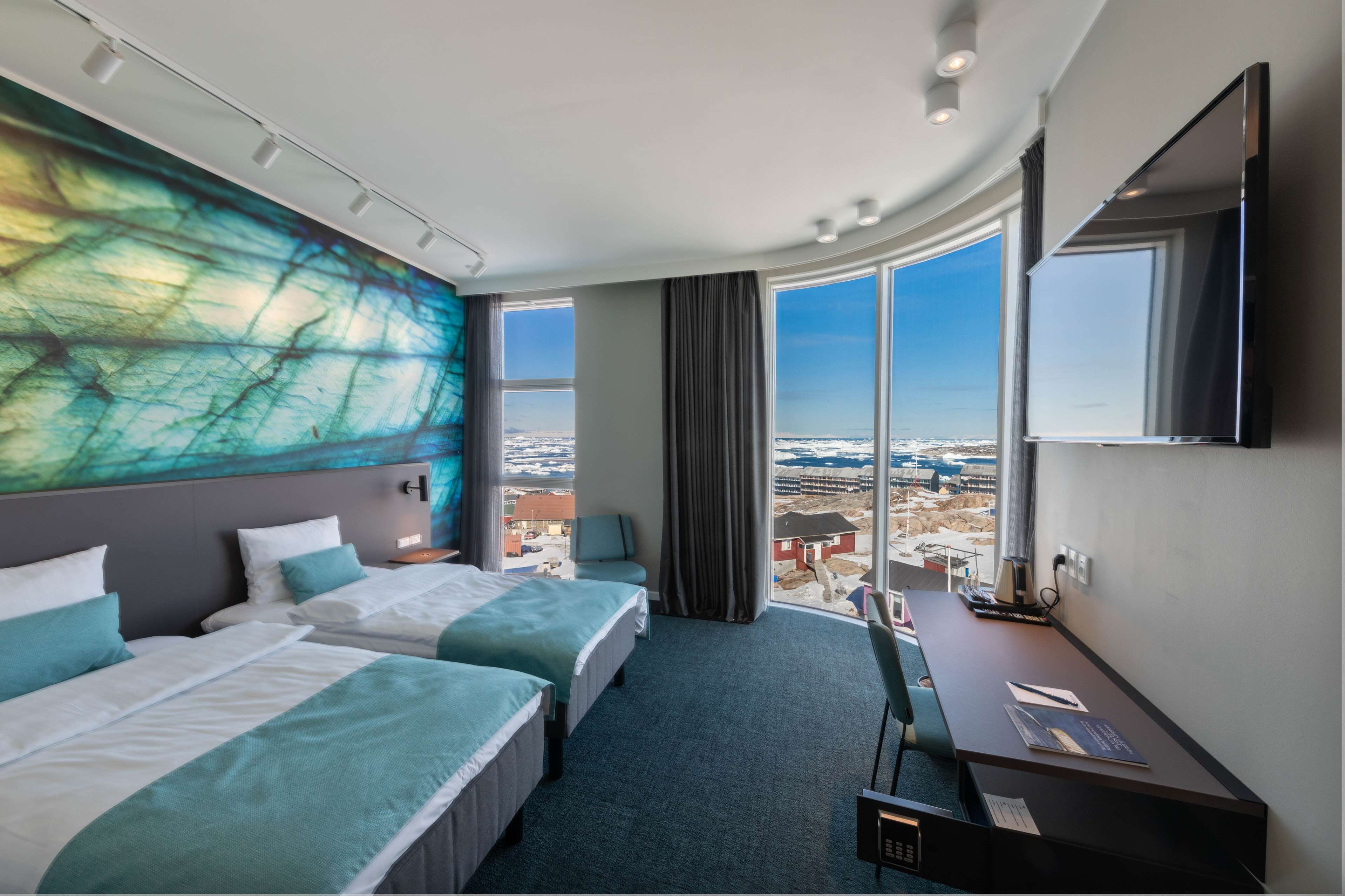 Habitación de hotel con dos camas, un escritorio, un televisor de pantalla plana y grandes ventanales con vistas a la ciudad.