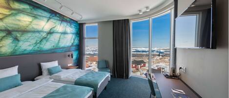 Habitación de hotel con dos camas, un escritorio, un televisor de pantalla plana y grandes ventanales con vistas a la ciudad.