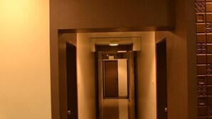 Un couloir étroit et bien éclairé, avec des portes de part et d’autre menant à un espace central.