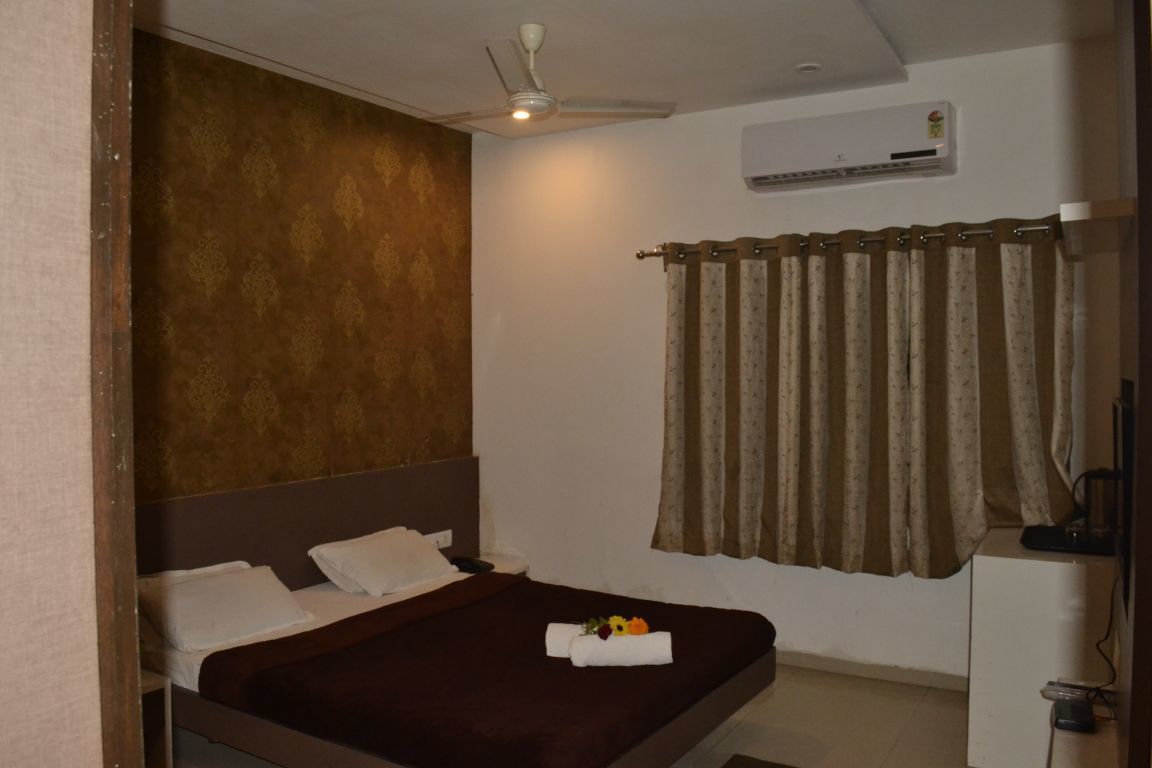 A single bed with a dark headboard, a ceiling fan, an air conditioning unit, and a curtain.