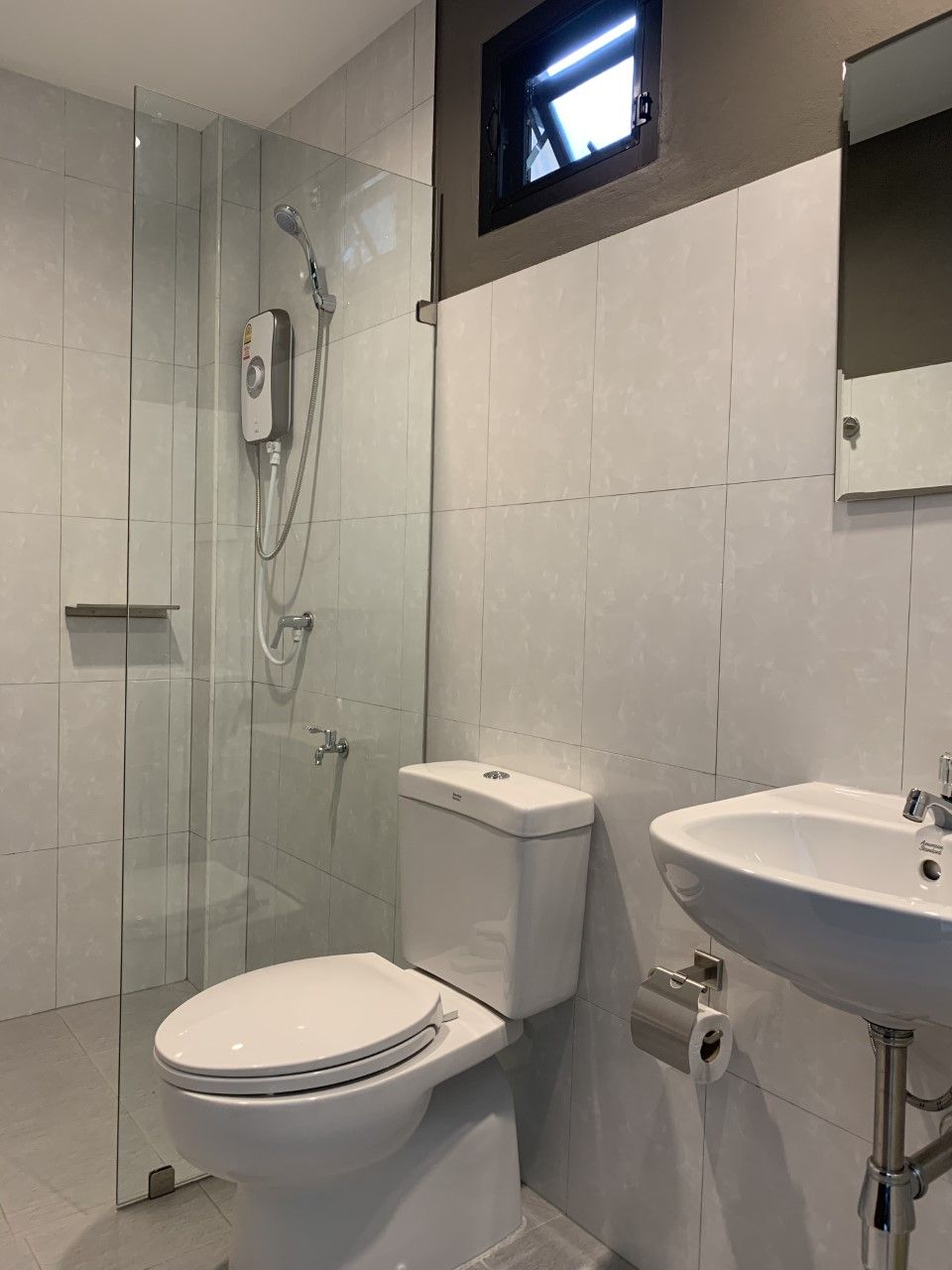 Ein modernes Badezimmer mit einer Duschkabine, einer weißen Toilette und einem Waschbecken mit Spiegel darüber.