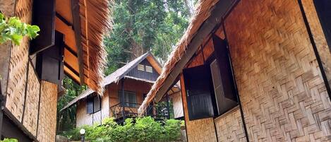 Une rangée de maisons traditionnelles en bois, coiffées de toits de chaume, entourées d’une végétation luxuriante.