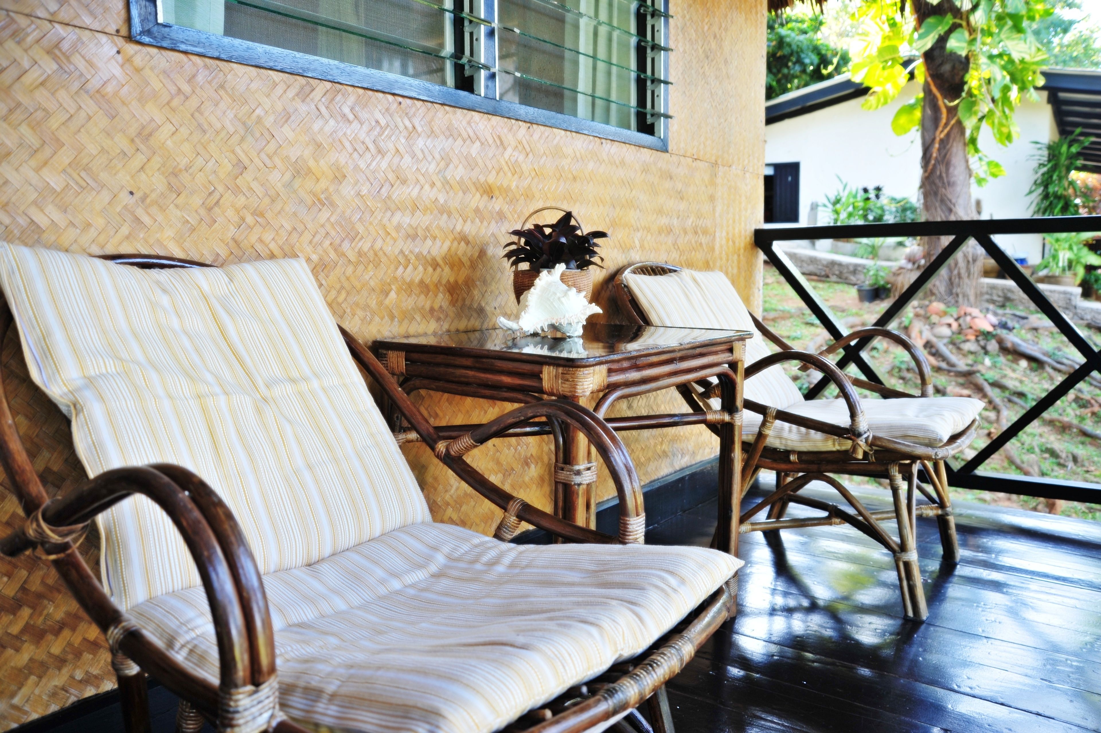 A wicker sofa and chairs on a wooden deck with a woven wall and a glass railing.