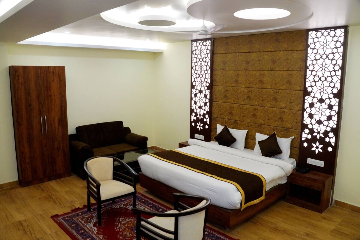 A hotel room with a bed, a sofa, a chair, a wardrobe, and a decorative wall panel.