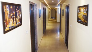 Un pasillo de hotel con cuadros enmarcados en las paredes, suelo pulido y puertas que dan a las habitaciones.