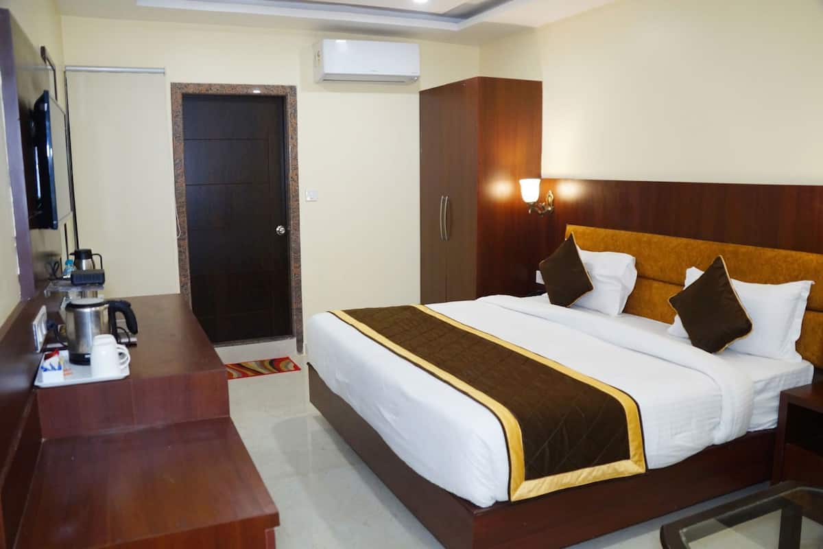 A hotel room with a bed, a desk with a coffee maker, a wardrobe, and an air conditioning unit.