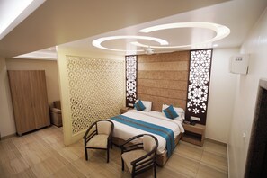 A modern hotel room with a bed, two chairs, a wardrobe, and decorative panels. - Hotel Shivoy Grand (Varanasi)