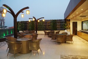 A rooftop terrace with wicker furniture, hanging lights, and a green wall with plants. - Hotel Shivoy Grand (Varanasi)